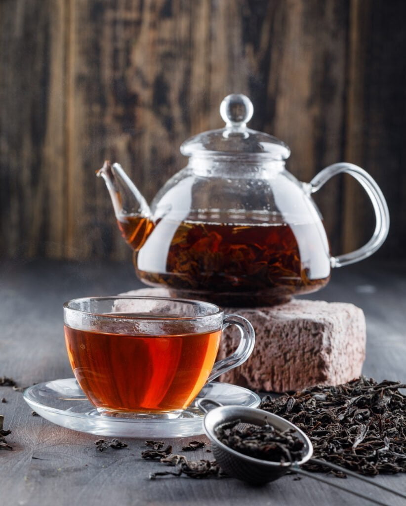 Black tea in teapot and cup with dry tea, brick side view on a wooden background